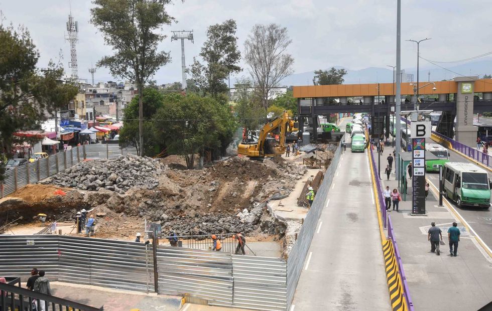 Construction site beside a roadway underpass with buses, workers, fences, and machinery.