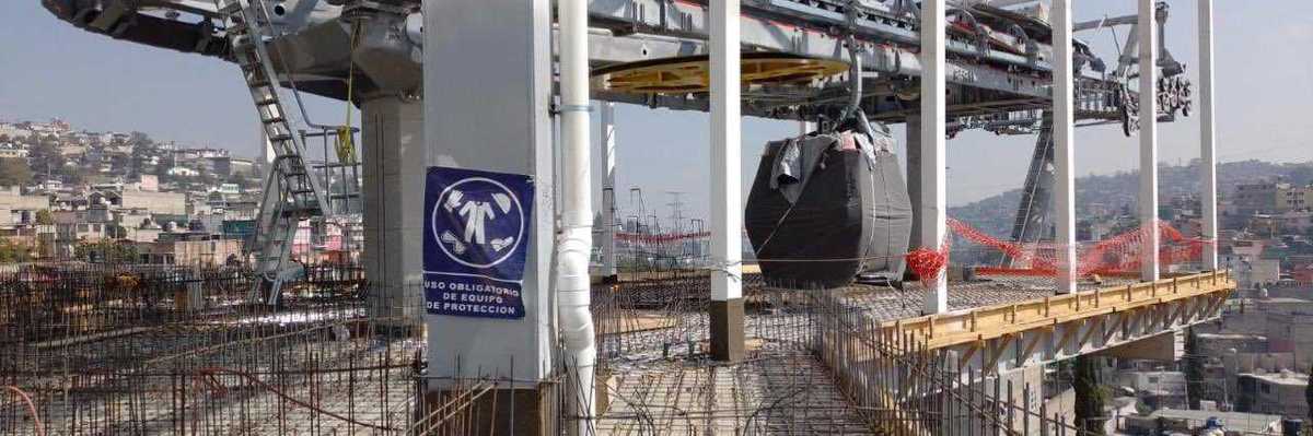 Construction site of an elevated cable car station with rebar and safety signage.
