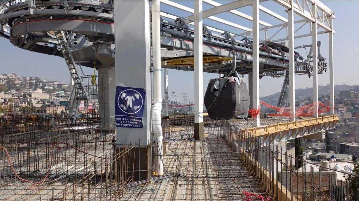 Construction site of an elevated cable car station with rebar and safety signage.
