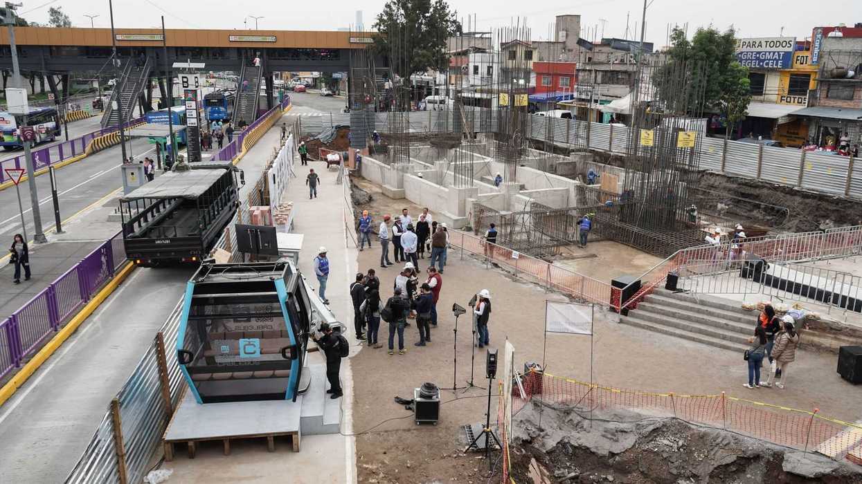 Construction site with people near a road, cable car station, and elevated walkway.