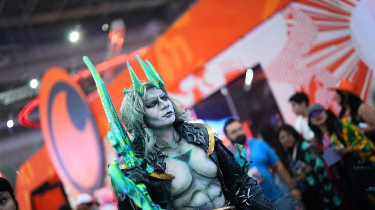 Cosplayer in elaborate armor with teal accents at a convention, orange backdrop.