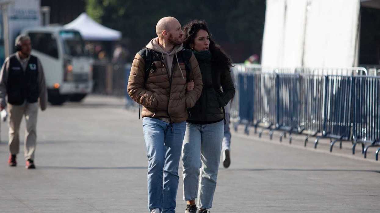 Couple walking arm in arm on a city street with metal barriers.