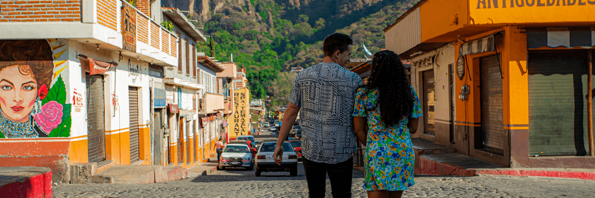 Couple walking on a sunny street with mountains in the background.