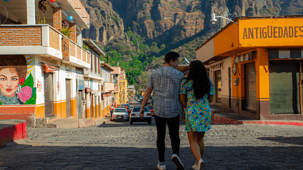 Couple walking on a sunny street with mountains in the background.