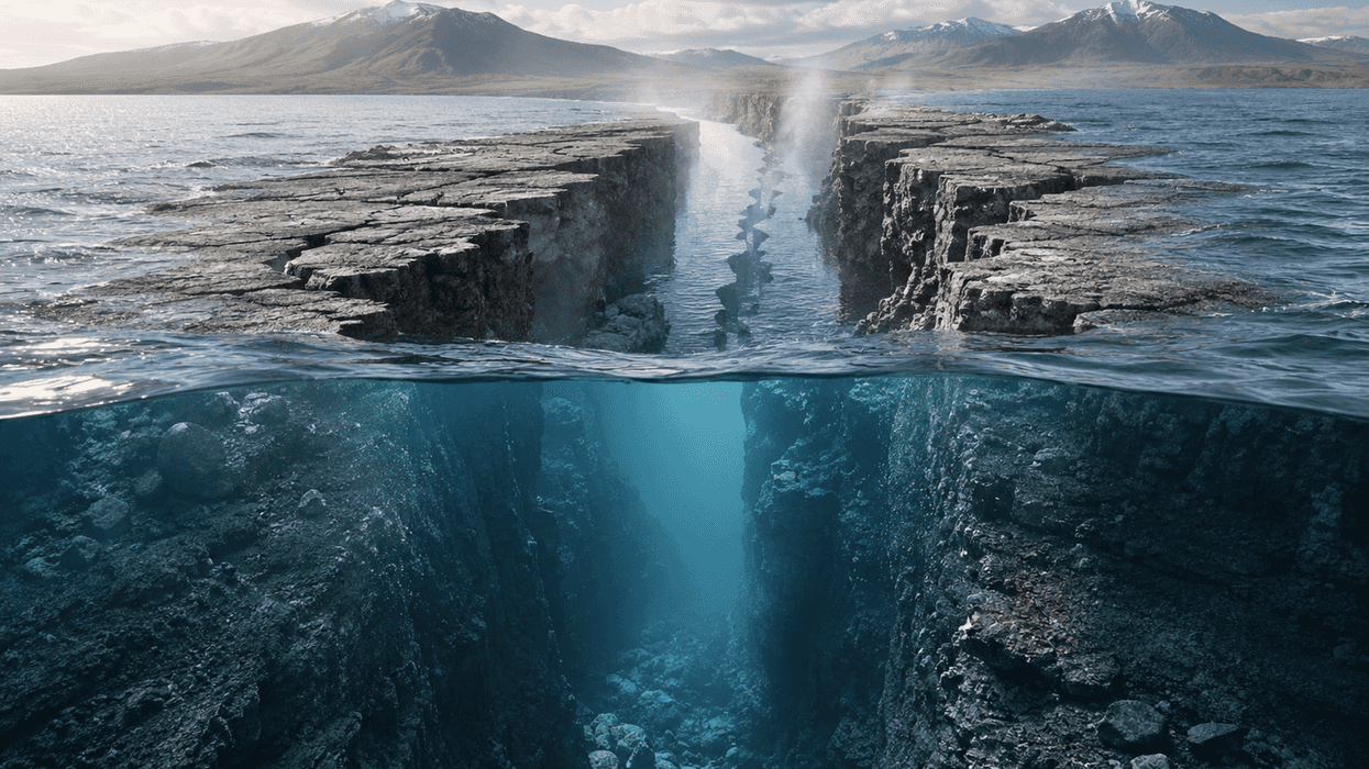 Cracked ocean floor with emerging steam and distant mountains under a clear sky.