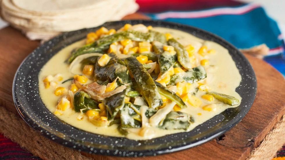 Creamy corn and poblano dish on a black plate, with folded tortillas beside it.