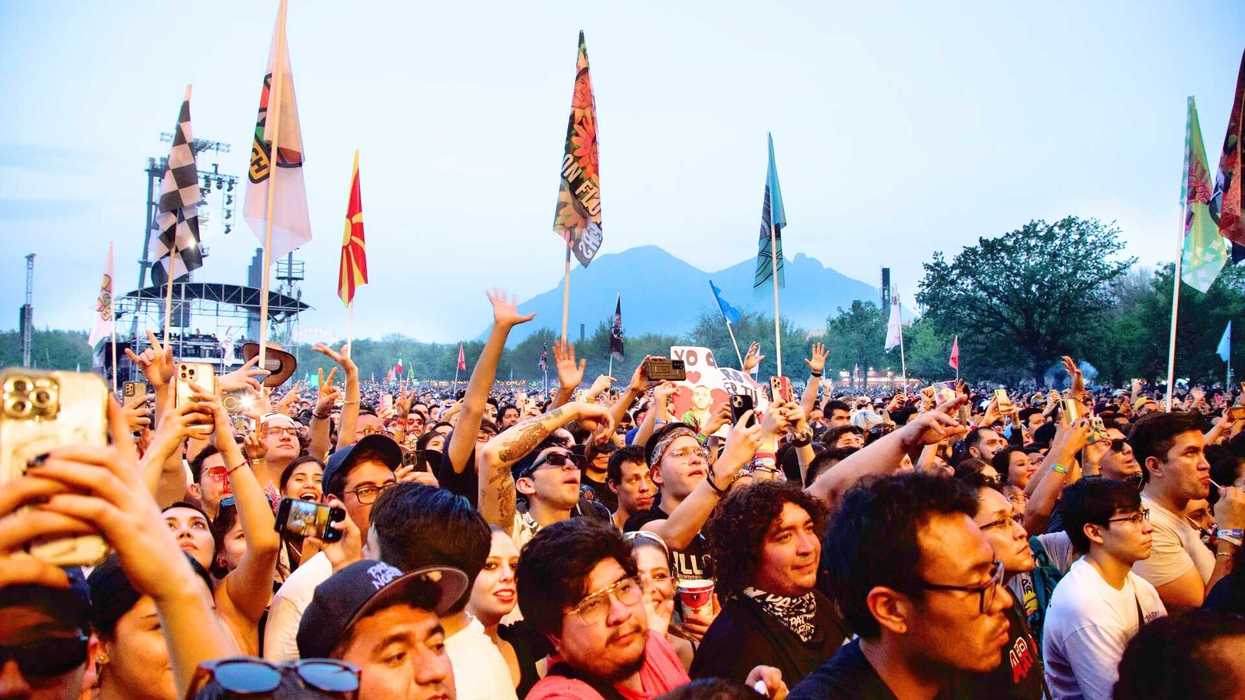 Crowd at an outdoor concert, waving flags and capturing moments on phones.