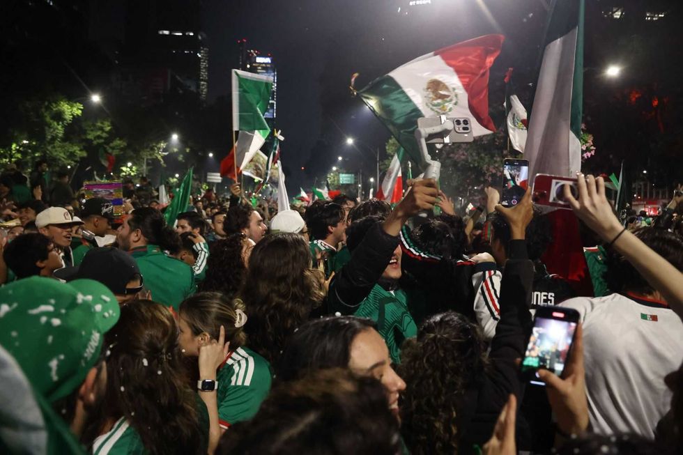 Crowd celebrating at night with Mexican flags and smartphones raised in the air.