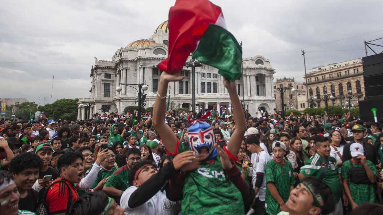Crowd celebrating in Mexico City, boy with Mexican flag and lucha mask, palace in background.