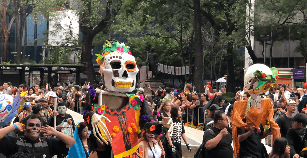 Crowd celebrating with colorful skeleton puppets during Day of the Dead parade.