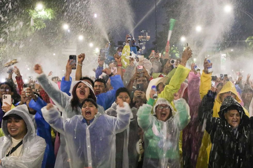 Crowd celebrating with joy, wearing rain ponchos under water spray, capturing moments with phones.