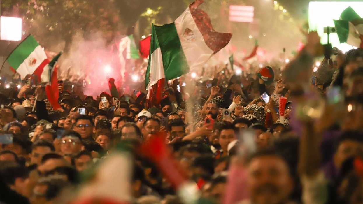 Crowd celebrating with Mexican flags and lights at night.