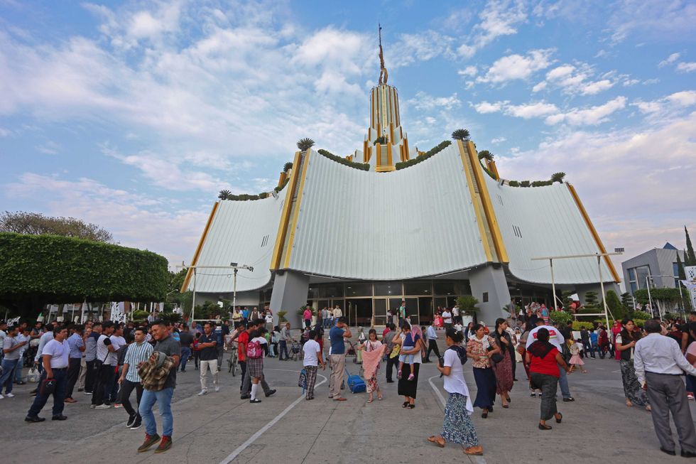 Crowd gathered outside a tall, ornate church with a golden spire on a sunny day.