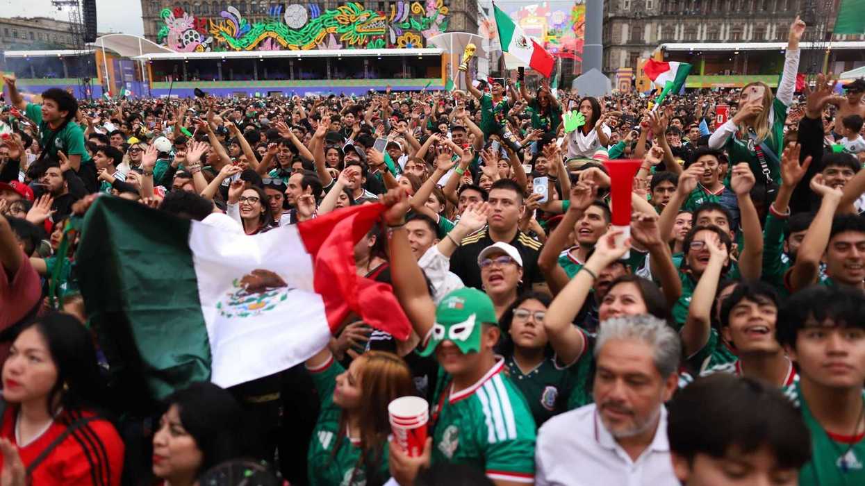 Crowd in Mexico City celebrates, holding flags and cheering, vibrant mural in the background.