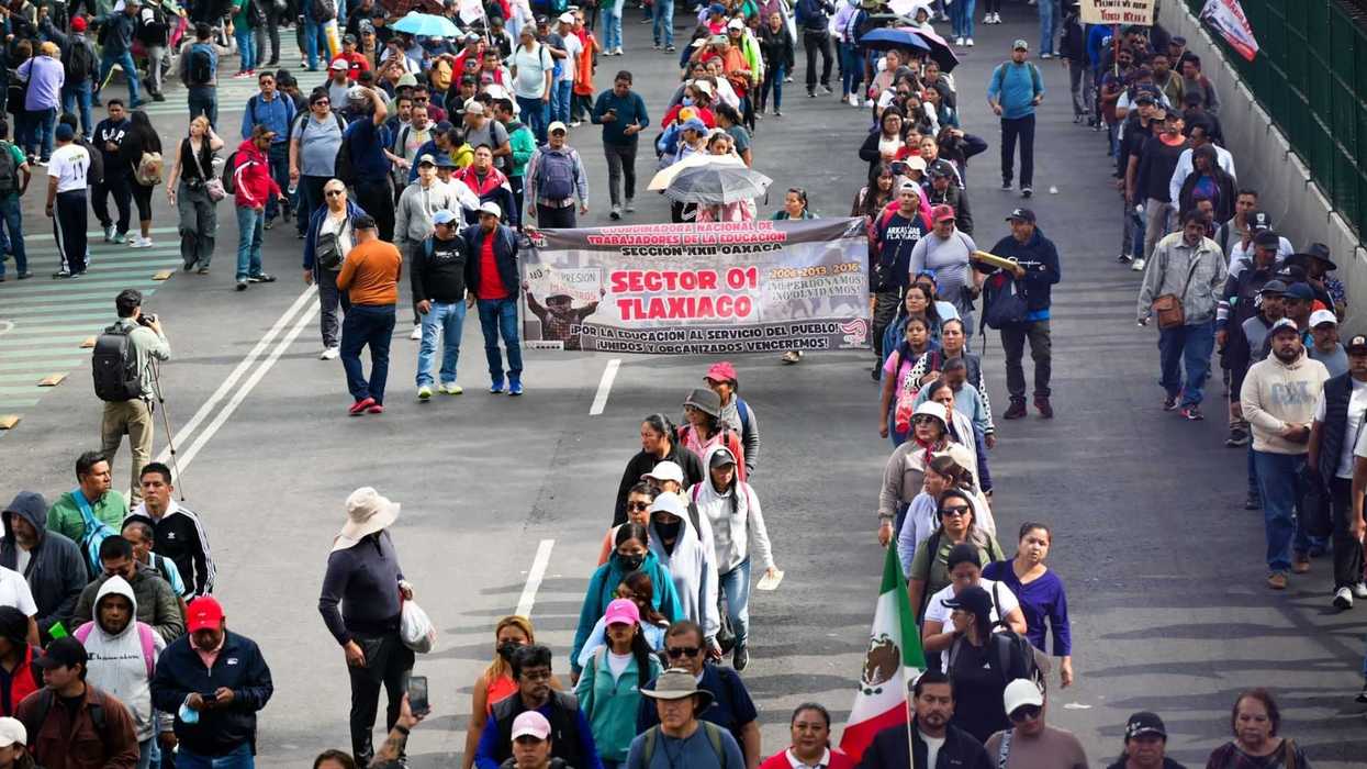 Crowd of people marching on a street, holding banners and a Mexican flag.