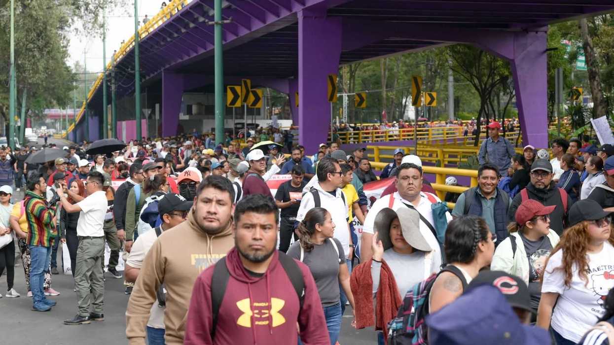 Crowd of people walking under a purple bridge during a protest or public gathering.