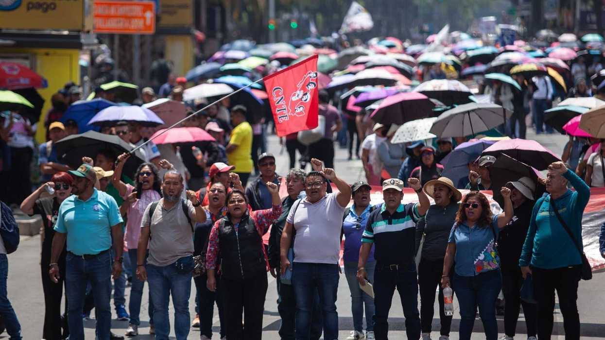 Crowd of protesters holding umbrellas and a red flag on a busy street.