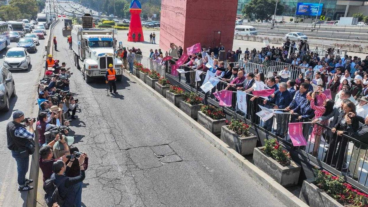 Crowd waves flags at truck on highway, photographers capture the scene in a busy urban area.