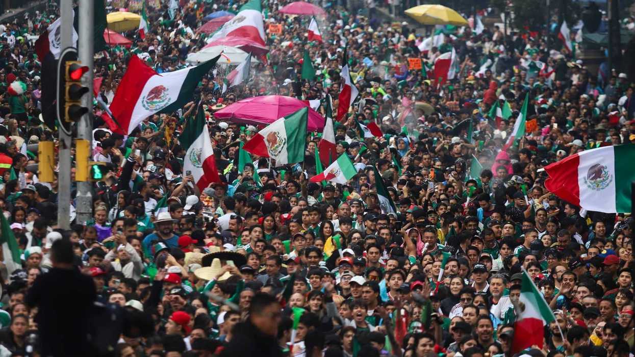 Crowd waving Mexican flags at a large street celebration.