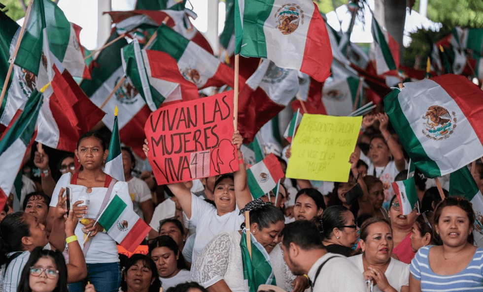 Crowd waving Mexican flags with signs supporting women at a rally.