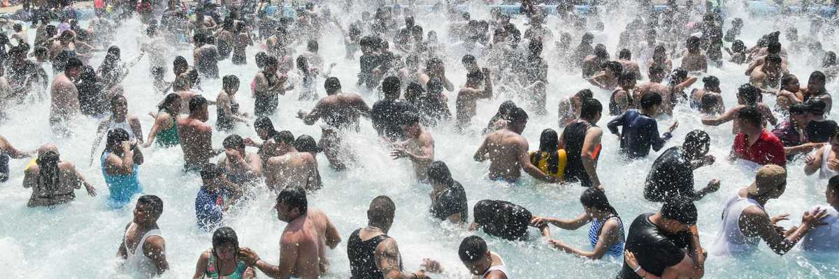 Crowded pool party with people splashing water and enjoying in the sun.