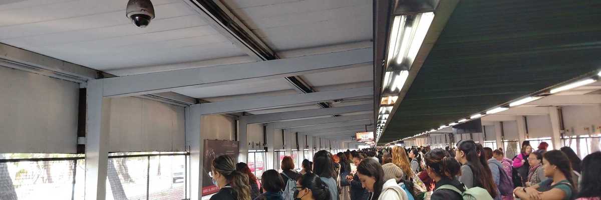 Crowded subway platform with people waiting under fluorescent lights.