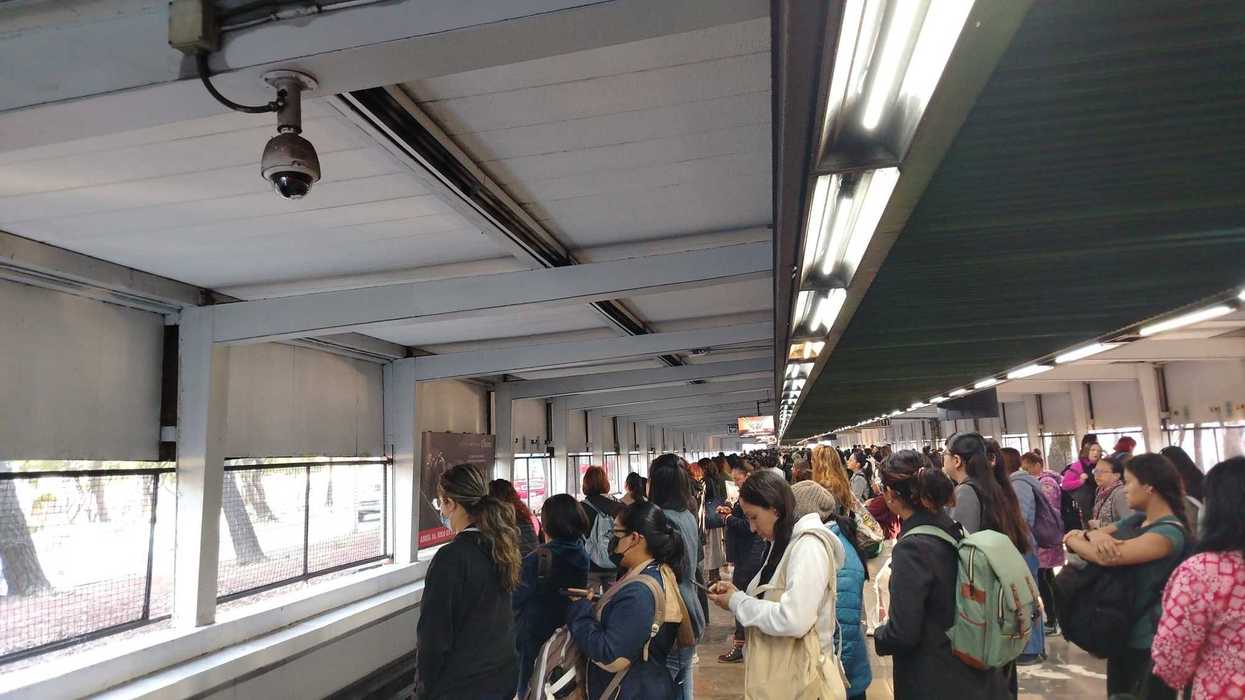 Crowded subway platform with people waiting under fluorescent lights.