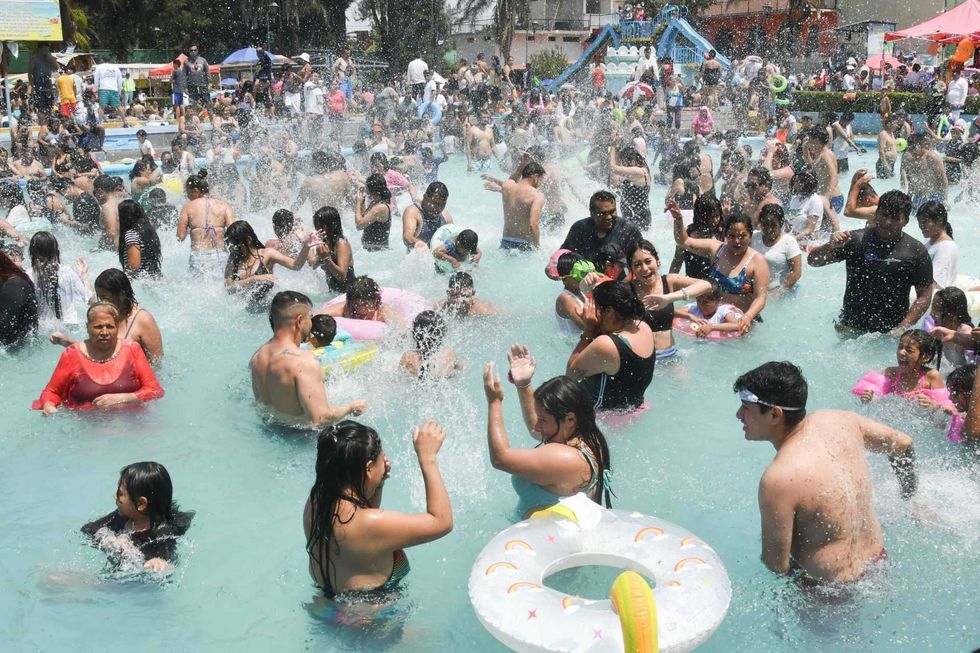 Crowded swimming pool with people splashing and playing in the water.