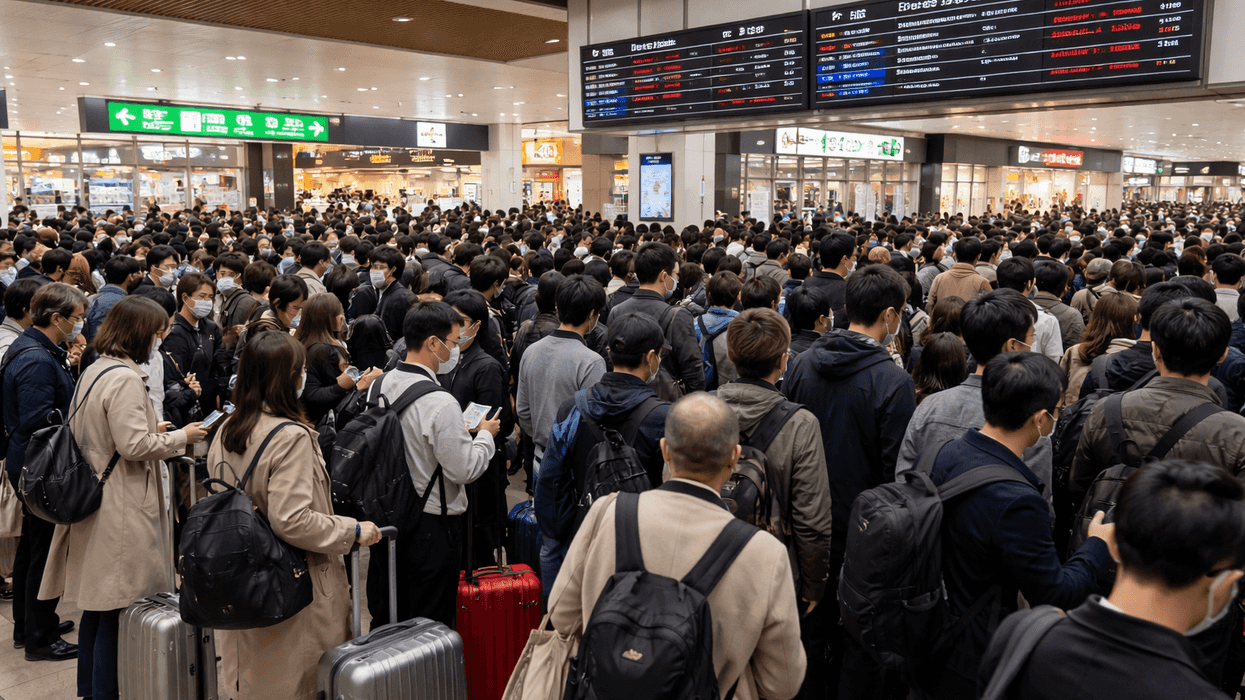 Crowded train station with people, luggage, and signboards overhead.