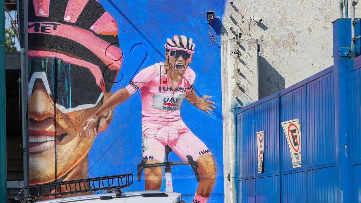Cyclist mural on a wall, featuring a rider in pink and sunglasses, next to a blue gate.