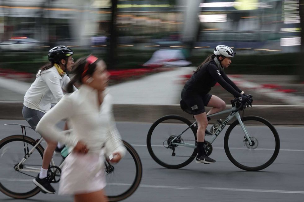 Cyclists riding quickly alongside a blurred pedestrian on a city street.