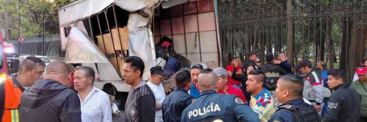 Damaged truck by a fence, surrounded by police and onlookers.