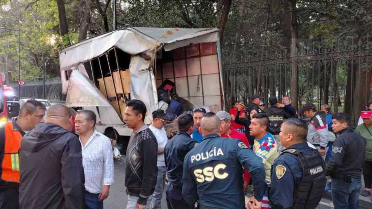 Damaged truck by a fence, surrounded by police and onlookers.
