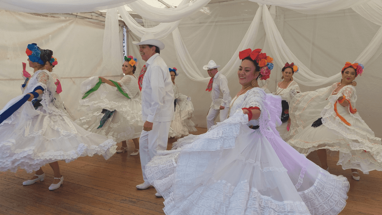 Dancers in traditional Mexican attire perform a lively dance under flowing white drapes.