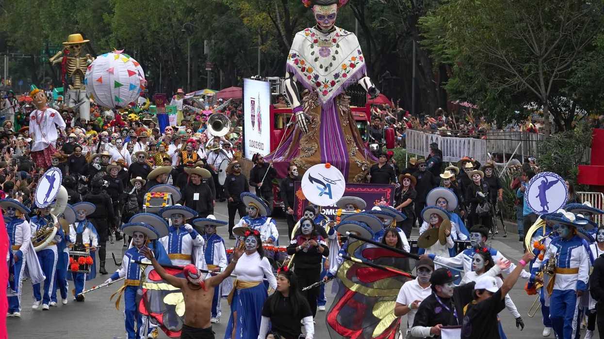 Day of the Dead parade with dancers, a large skeleton figure, and colorful costumes.
