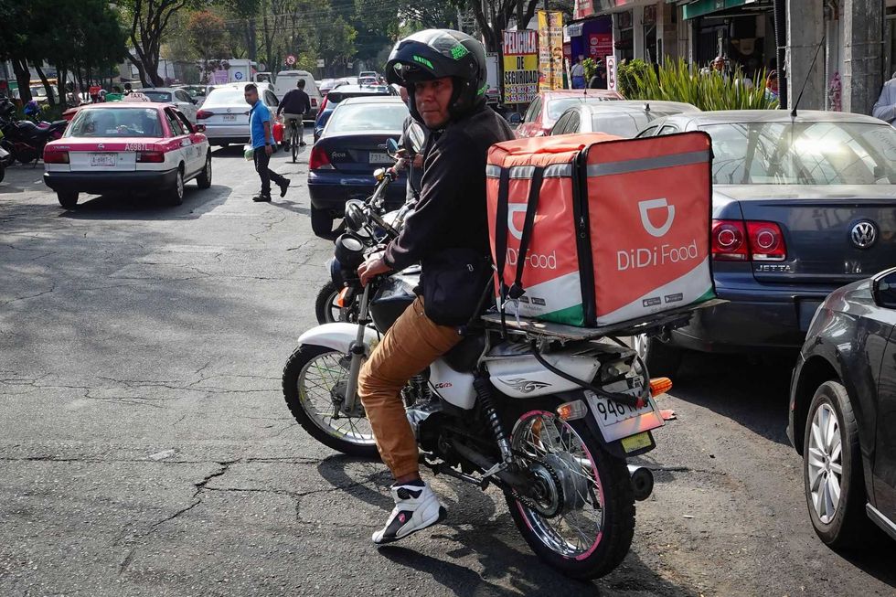 Delivery worker on motorcycle with DiDi Food bag in busy street scene.