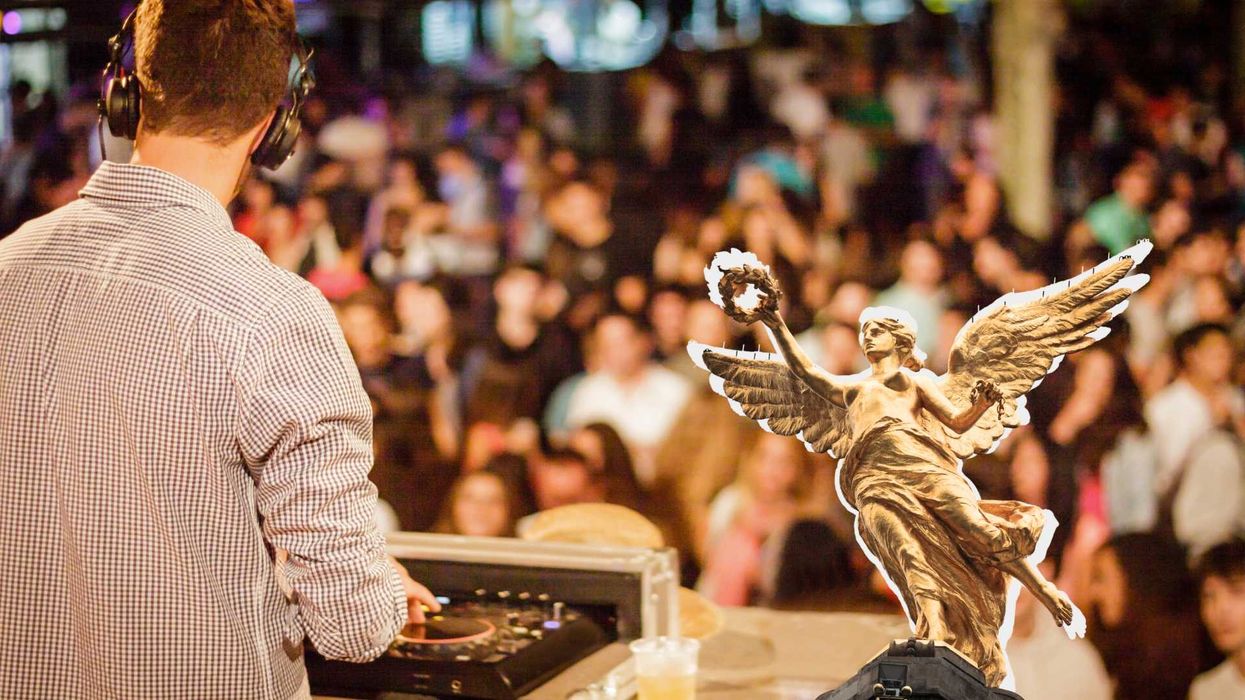 DJ performing for a large crowd, with a winged statue in front.