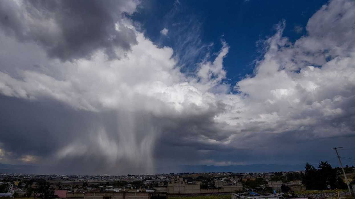 Dramatic sky with rain falling over a cityscape, surrounded by dark and cumulus clouds.