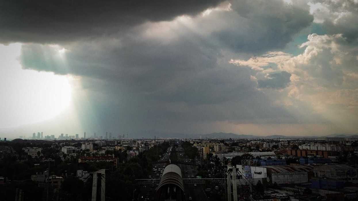 Dramatic skyline with rays of light breaking through dark storm clouds over a cityscape.