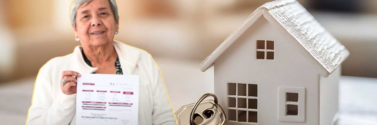 Elderly woman holding a document next to a miniature house and key on a table.
