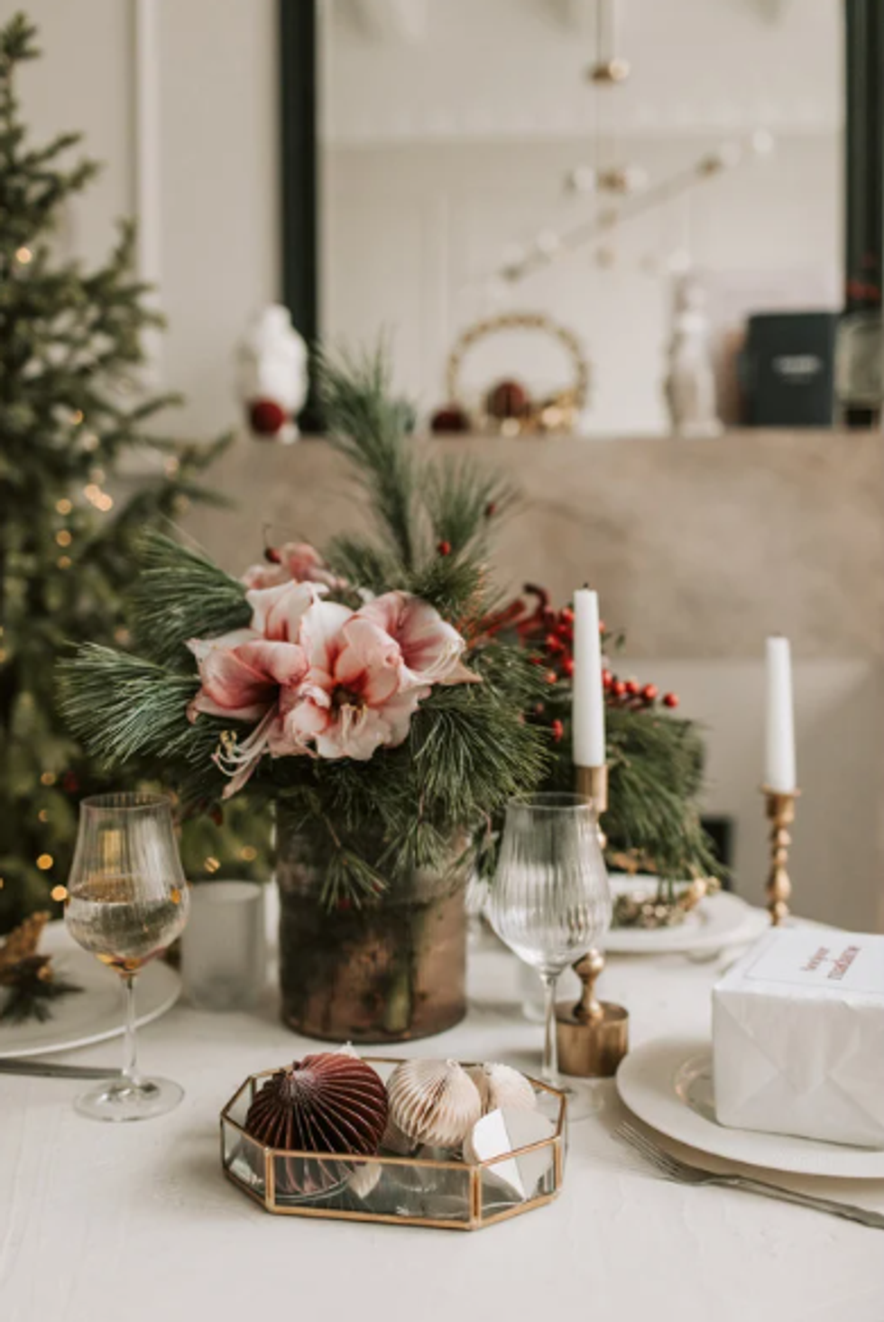 Elegant holiday table with floral centerpiece, candles, ornaments, and glasses.