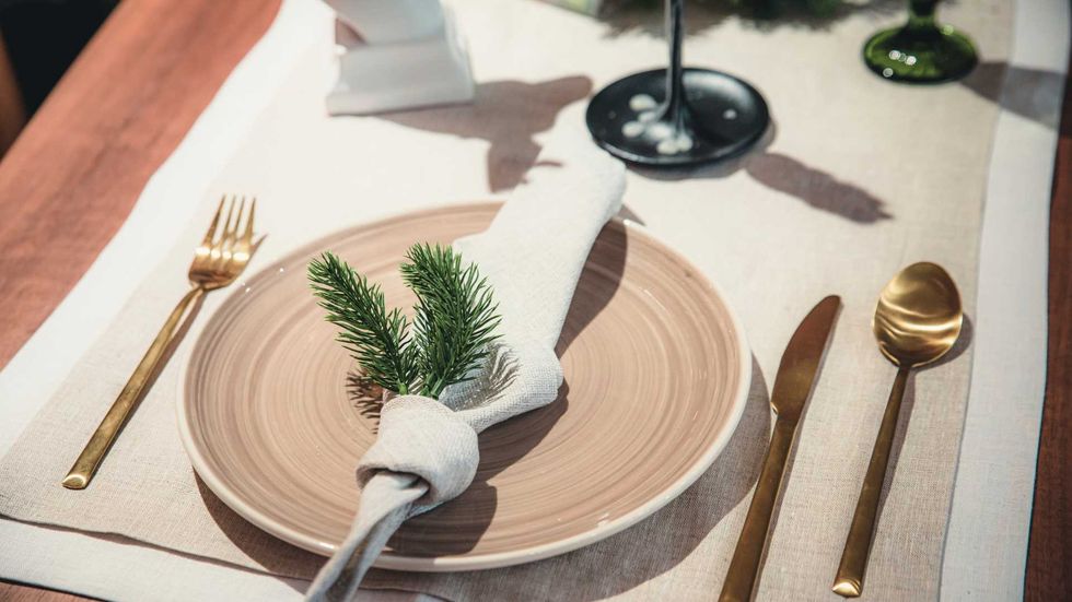 Elegant table setting with gold cutlery, napkin, and greenery on a beige plate.