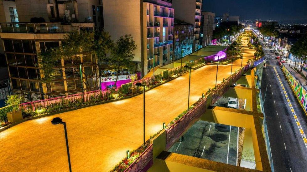 Elevated, illuminated pathway with trees alongside a city street at night.