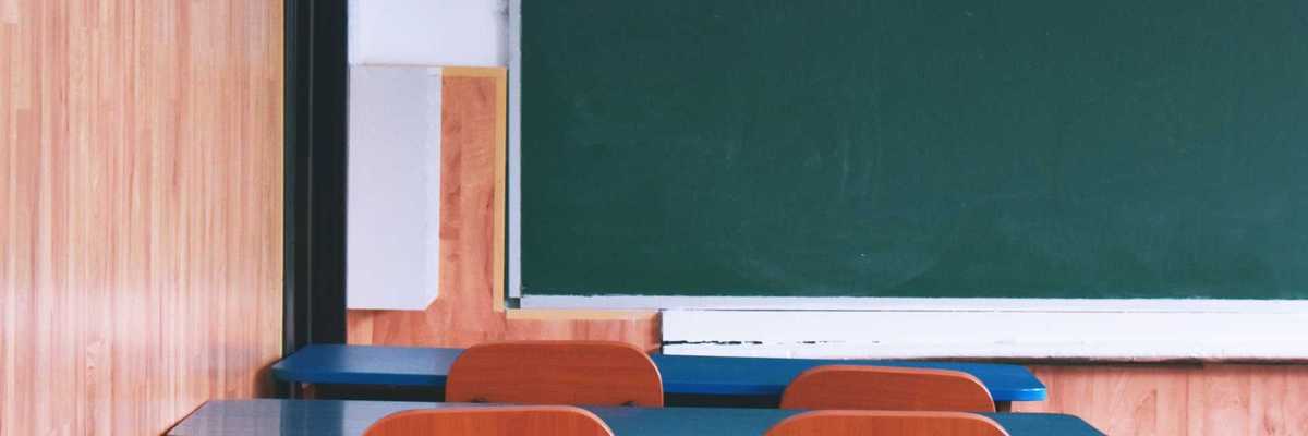 Empty classroom with wooden desks and a large green chalkboard.