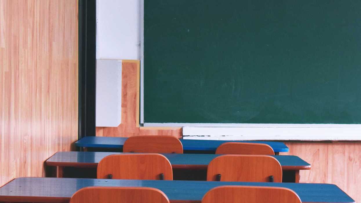 Empty classroom with wooden desks and a large green chalkboard.