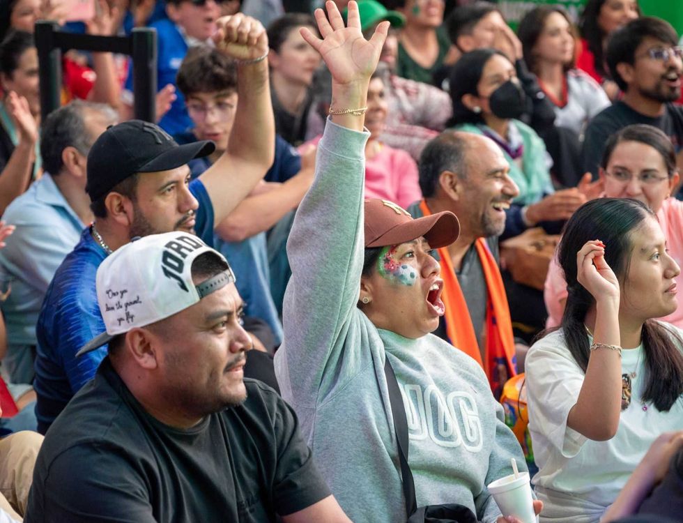 Enthusiastic crowd cheering, woman with face paint raising hand in excitement.