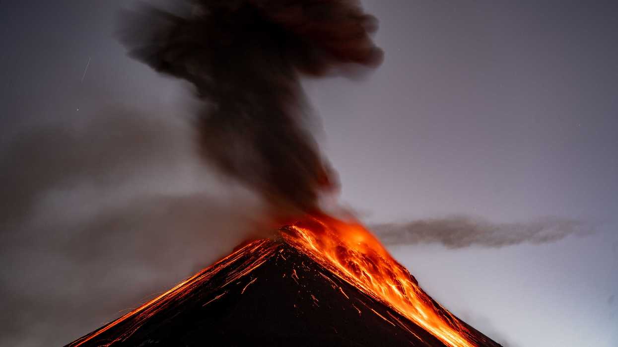 Erupting volcano at dusk, spewing lava and thick smoke into the sky.