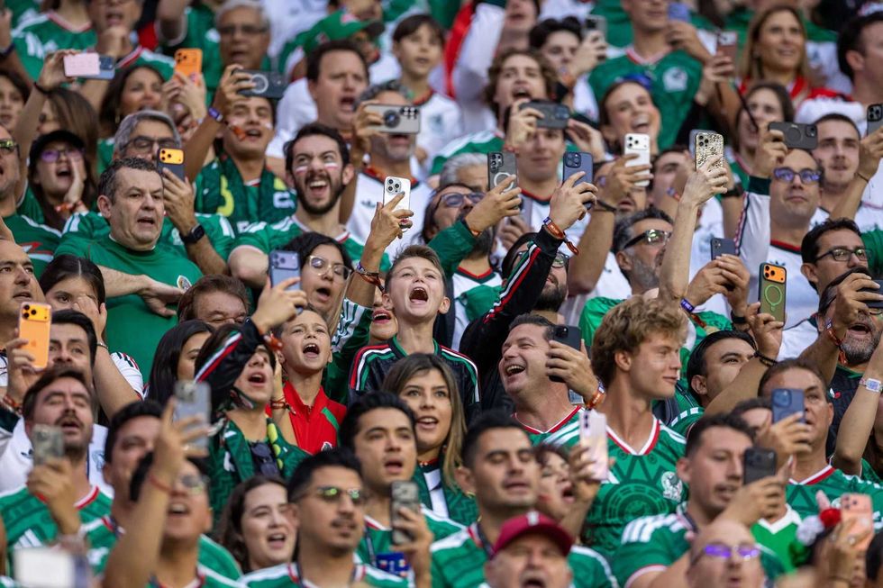 Excited crowd at a sports event, wearing green jerseys, capturing moments on phones.