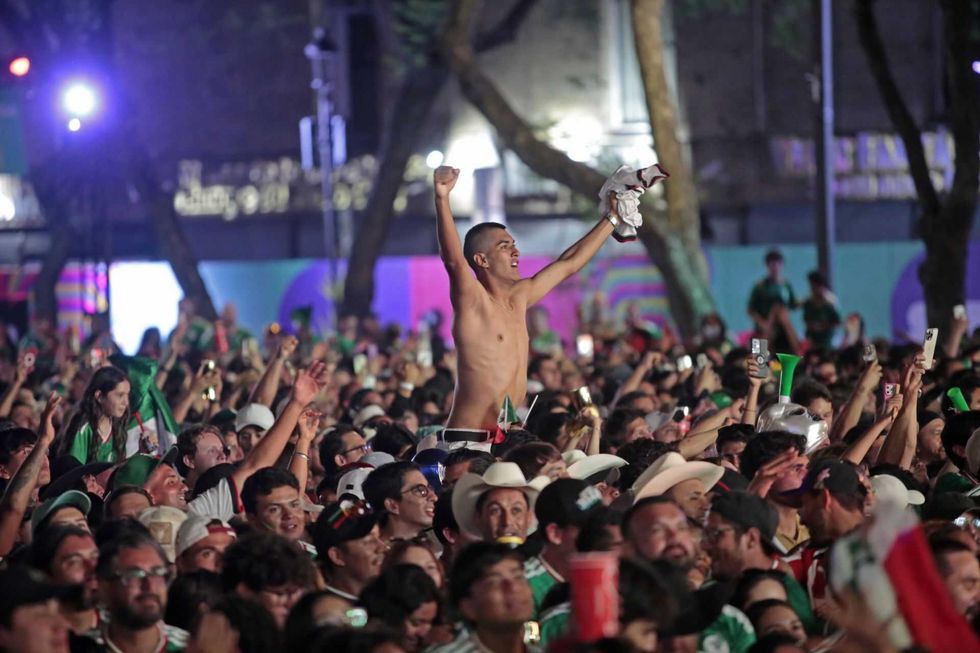 Excited crowd celebrating outdoors, man raised above others cheering with arms up.