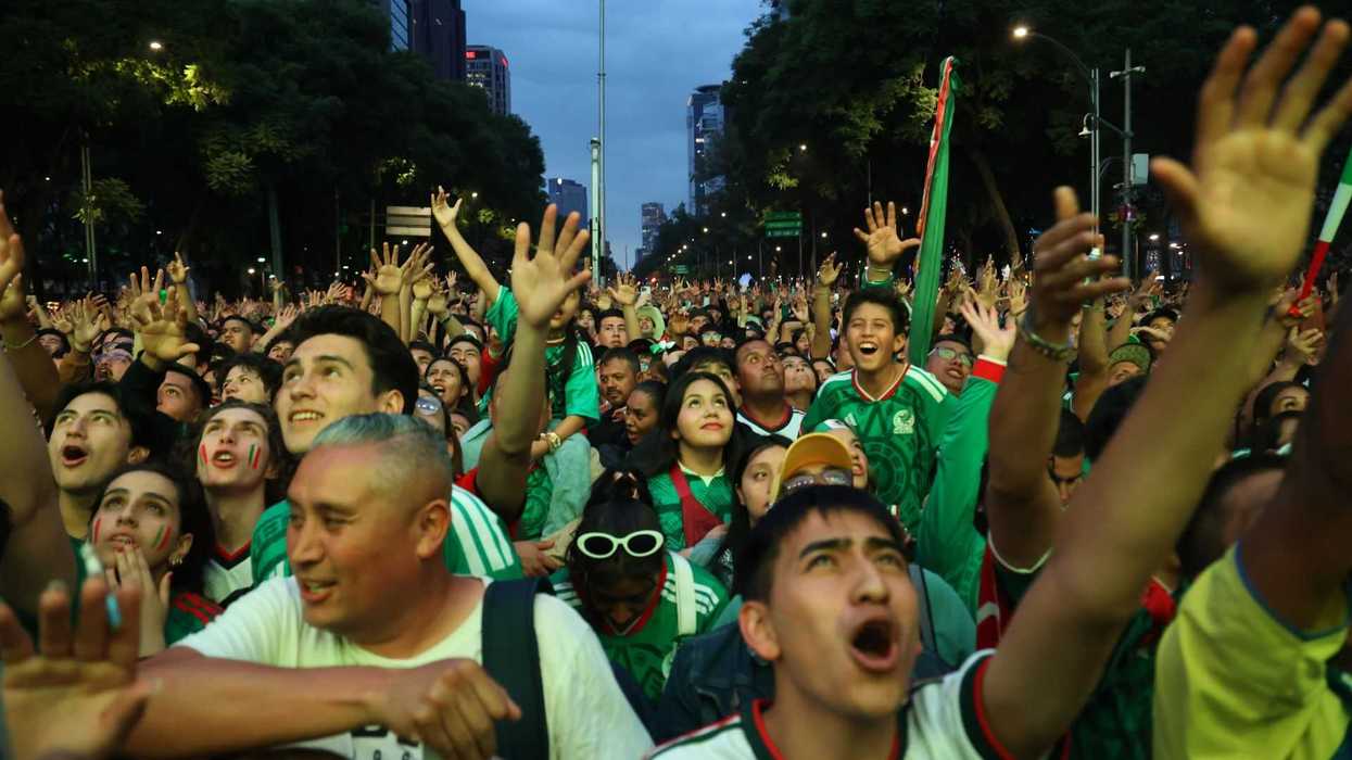 Excited crowd wearing green, cheering at an outdoor event during twilight.